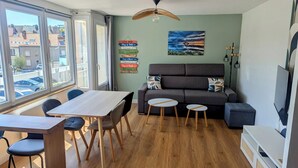 Un salon moderne avec un canapé, une table à manger et des chaises. Une grande fenêtre offre une vue sur la rue.