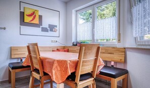 Un comedor con mesa y sillas de madera, una ventana con cortinas blancas y un cuadro en la pared.