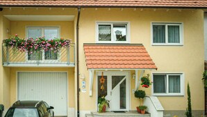 A two-story residential building with a red-tiled roof, a balcony with hanging flowers, and a front door with a small porch. - Apartment 'Marita Sigg' with Private Terrace, Shared Garden and Wi-Fi (Rust)