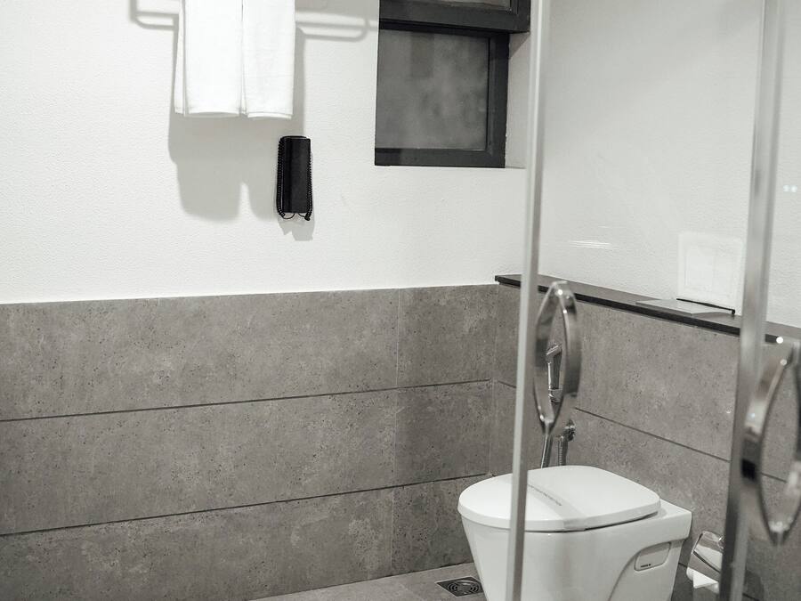 A modern bathroom with a glass shower enclosure, a white toilet, and a towel rack with folded towels.