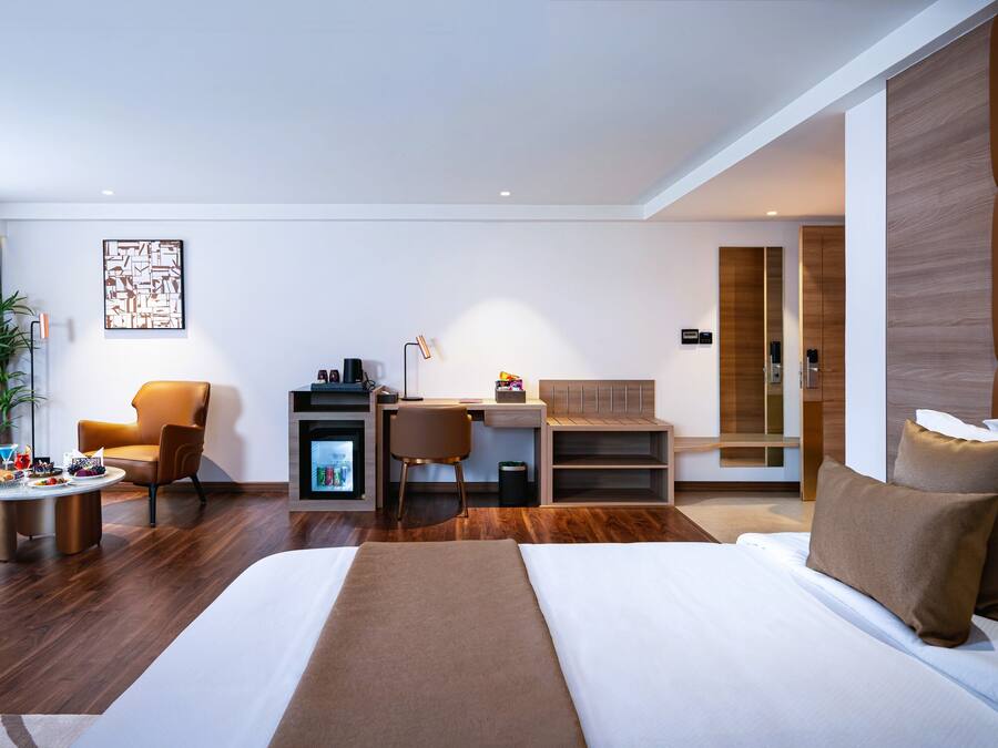 Una habitación de hotel moderna con una cama grande, un escritorio, una silla y una mesita con aperitivos.