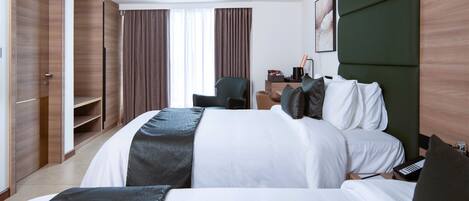 A hotel room with two beds, a desk, a chair, and a wardrobe.