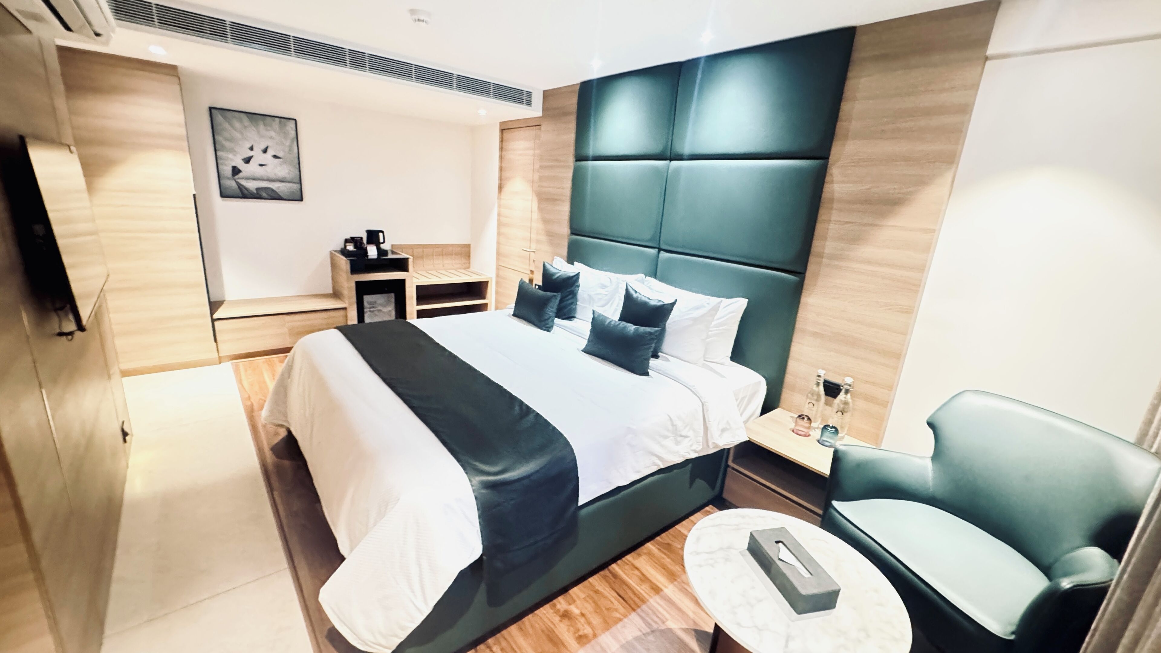 Une chambre d’hôtel moderne avec un grand lit, une table de chevet avec une lampe, une petite table ronde et une chaise.