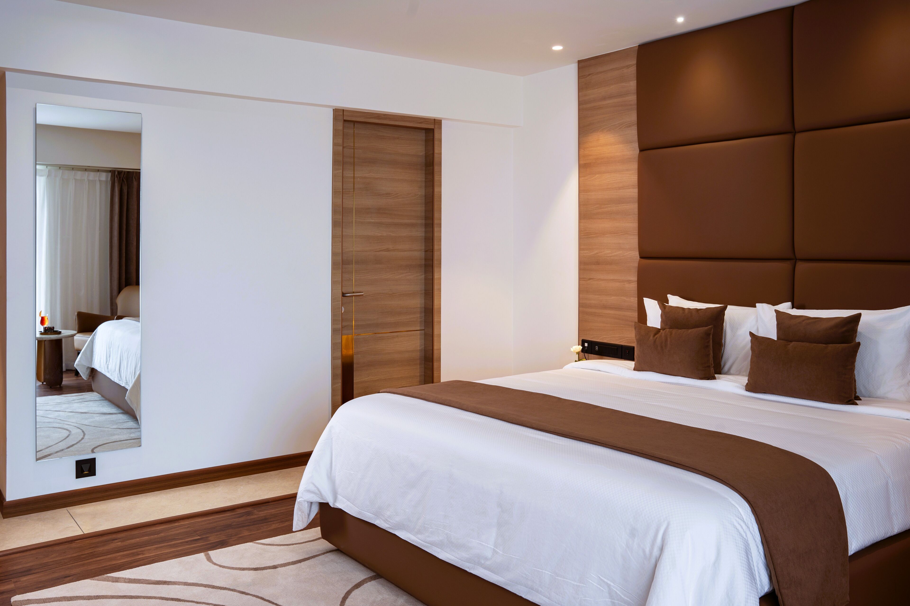Habitación de hotel moderna con una cama grande, cabecera de madera, un espejo y un armario de madera.