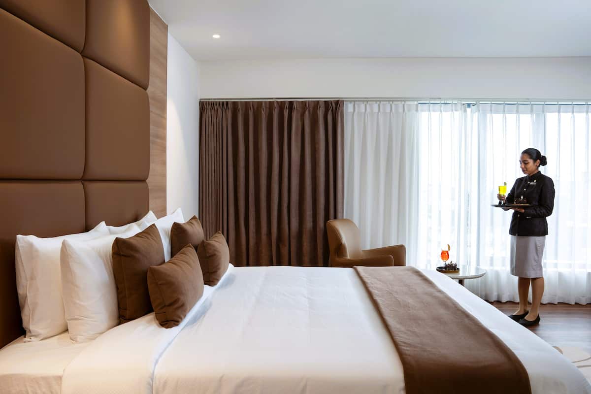 Ein Hotelzimmer mit einem großen Bett, einem Nachttisch, einem Sessel und einem Fenster mit Vorhängen.
