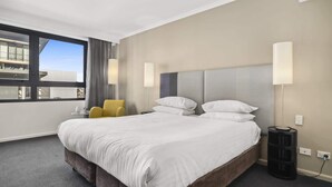 A hotel room with a large bed, two bedside lamps, a chair, and a view of buildings through a window. - Mantra Parramatta Studio with Pool Access (Parramatta)