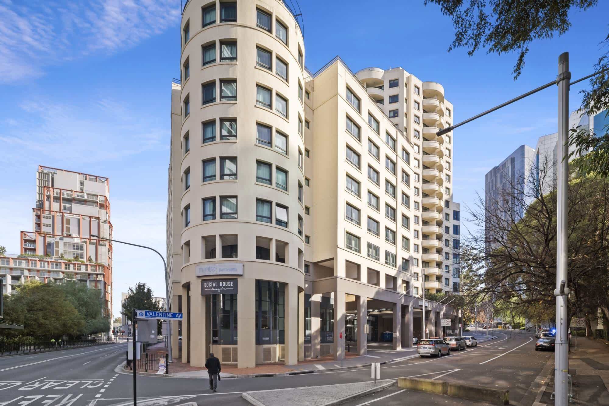 A modern hotel with a curved facade, multiple balconies, and a sign for a social house.