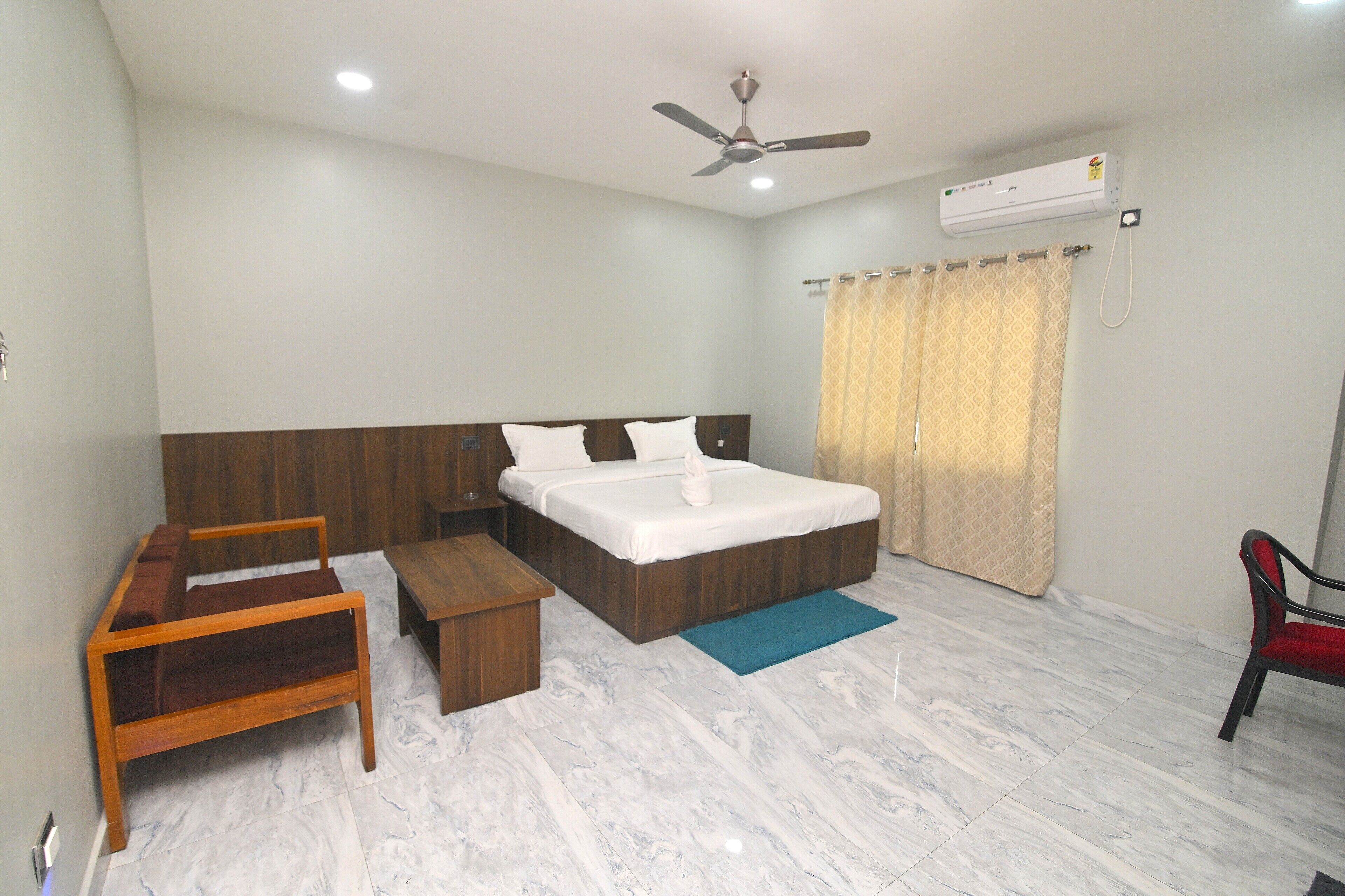 A bedroom with a bed, a wooden bench, a small table, a ceiling fan, and an air conditioning unit.