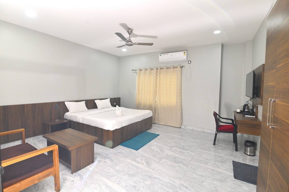 A hotel room with a bed, a desk, a chair, a ceiling fan, and an air conditioning unit.