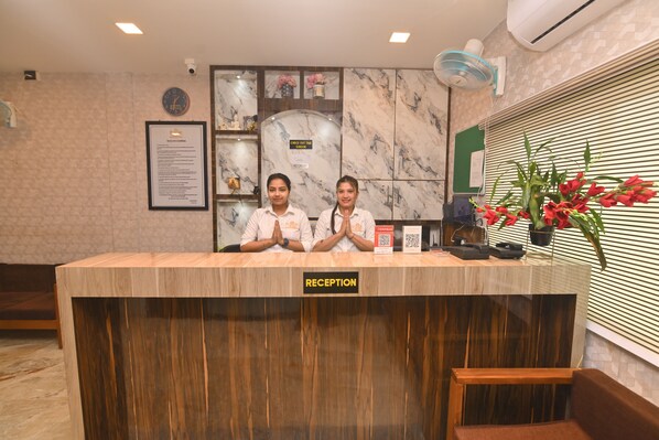 A reception desk with two staff members, a clock, and a framed document on the wall. - The Siam Hotel (Sonari)