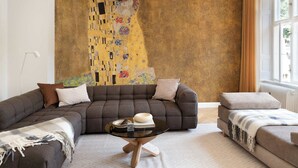 A modern living room with a large abstract painting, a sectional sofa, a coffee table, and a window with curtains. - Former Dukes Residence - 4 bedrooms - 2 bathroms (København)