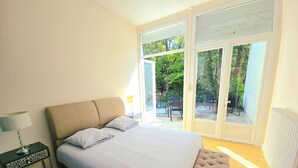 A bedroom with a bed, nightstand, and a view of the outdoors through a sliding door. - LES LOGIS DU CHATEAU MARIE VICTORIA on the way to ST-JACQUES-DE-COMPOSTELLE (La Vergne (17400))