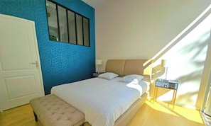 Une chambre à coucher avec un lit, un banc, une table de chevet, une fenêtre et une porte.