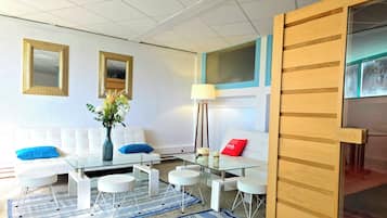 Un salon moderne avec un canapé blanc, des coussins bleus, une table basse en verre et un vase rempli de fleurs.
