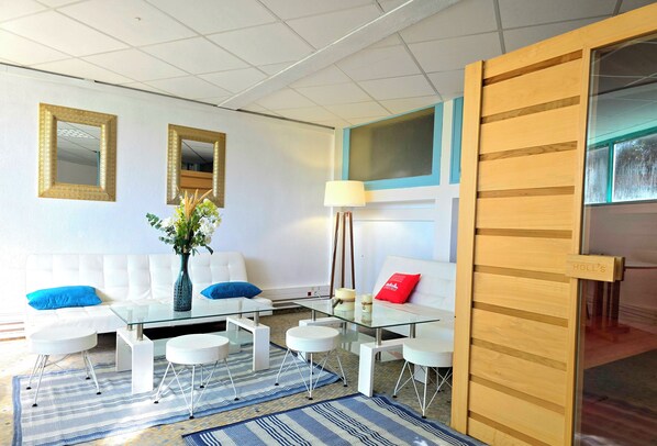 A modern living room with a white sofa, blue cushions, a glass coffee table, and a vase with flowers. - LES LOGIS DU CHATEAU MARIE VICTORIA on the way to ST-JACQUES-DE-COMPOSTELLE (La Vergne (17400))