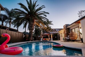 A backyard with a swimming pool, a palm tree, and a flamingo float.