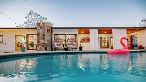 A swimming pool with a pink flamingo float, wicker chairs, and a stone wall. - Central SD• Luxury Home+Casita, Pool•Hot tub•BBQ•Sleeps10 (La Mesa)