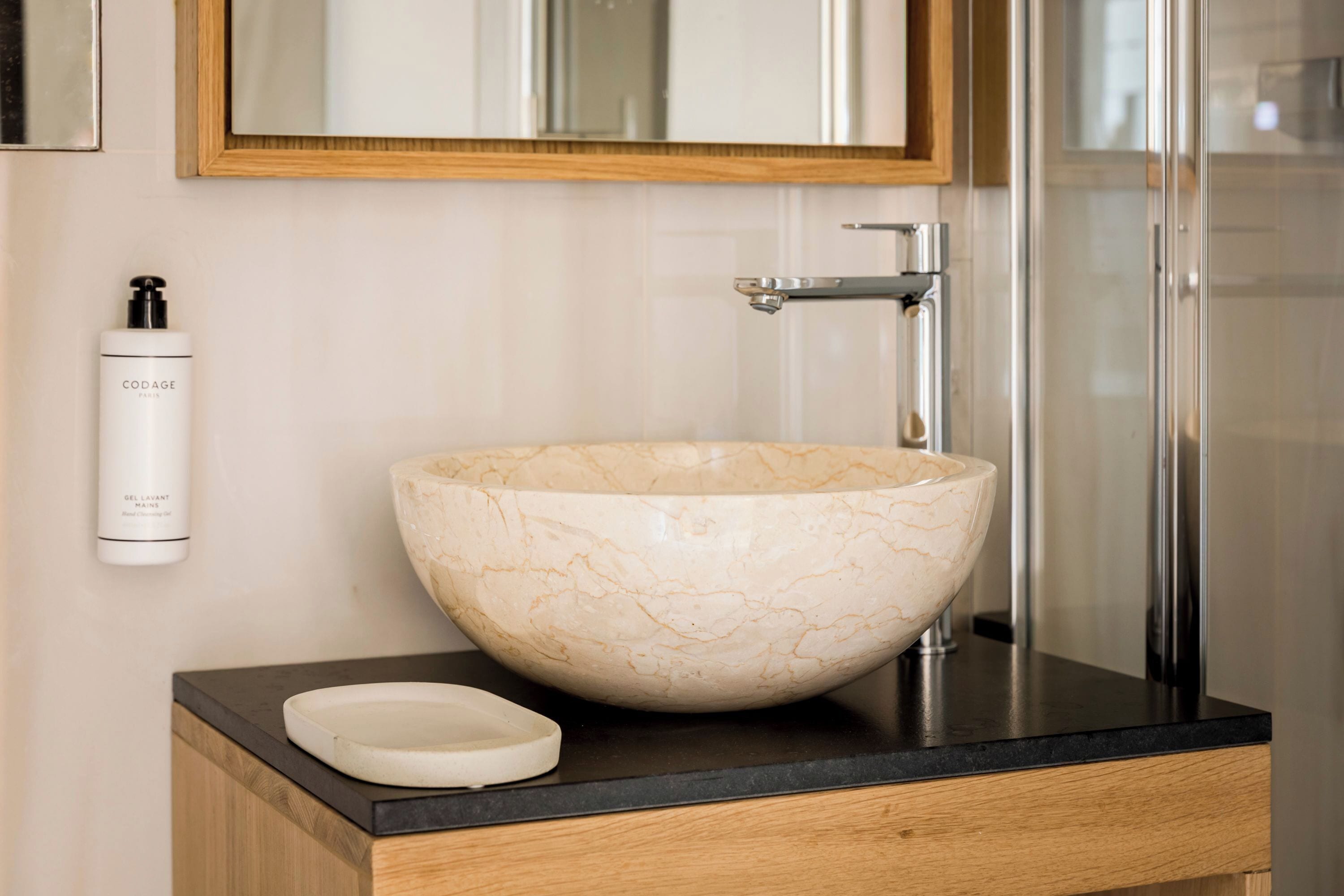 Un baño con lavamanos de mármol, un mueble de madera y un espejo sobre el lavamanos.