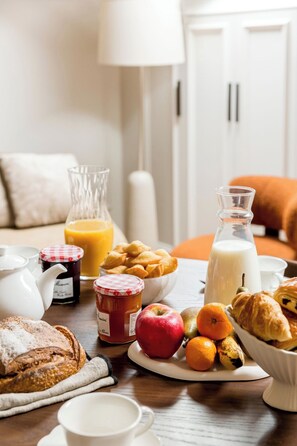 A breakfast table with various food items, a jug of milk, a glass of orange juice, a jar of jam, and a loaf of bread. - Merveil Luxury Suites - Cyr I-II - Terrasse (Paris)