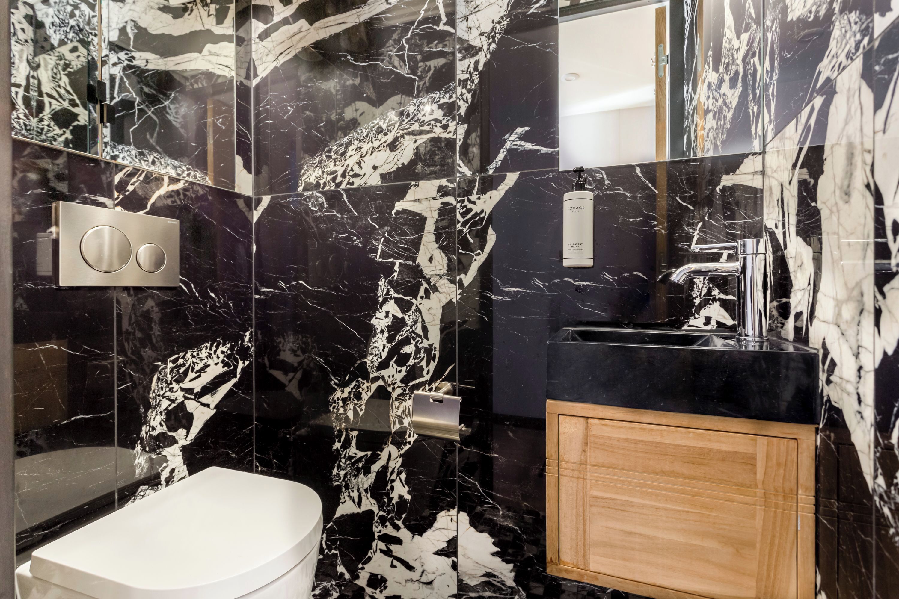 A modern bathroom with a marble backsplash, a white toilet, a black sink, and a wooden cabinet.