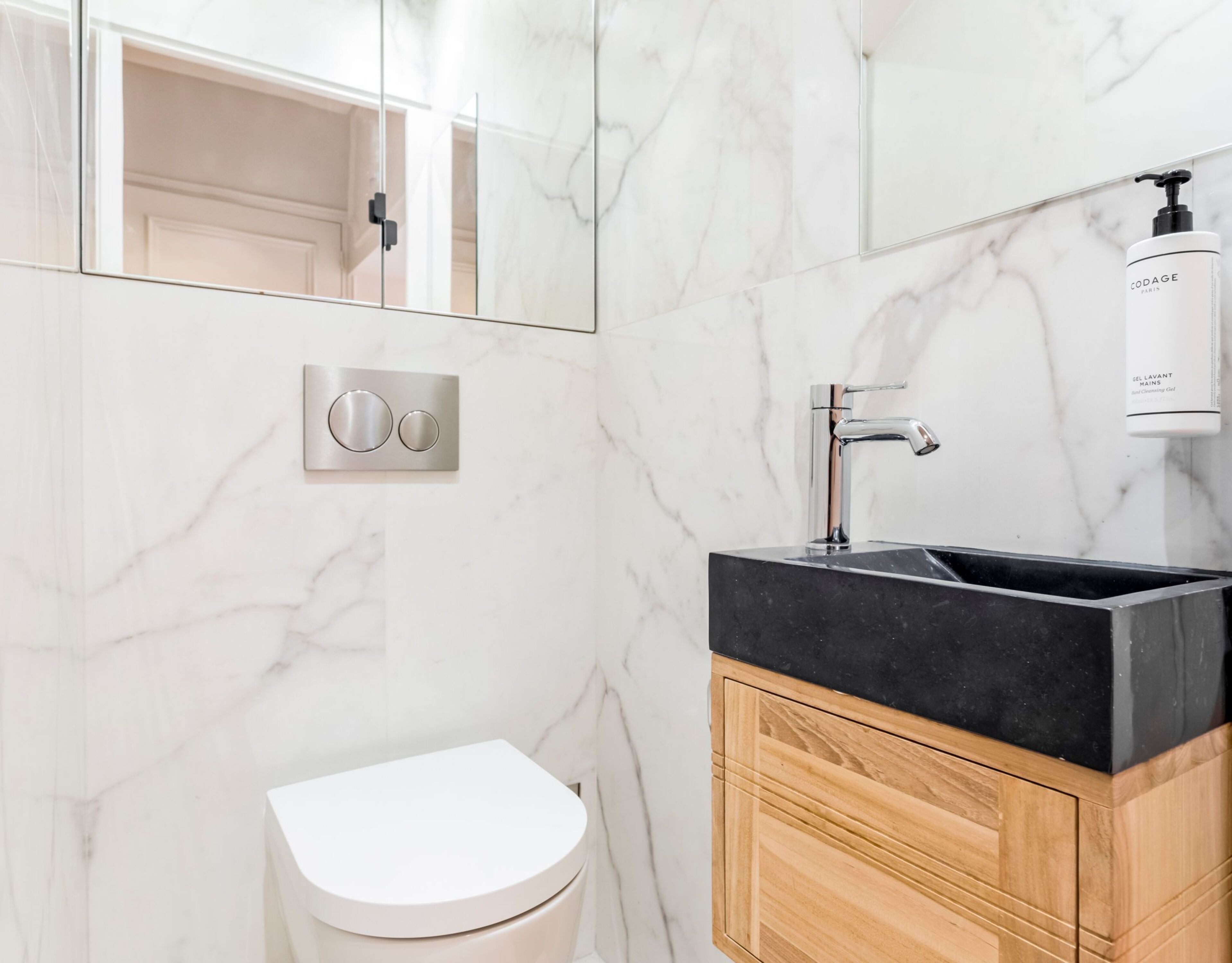 A modern bathroom with a marble wall, a black sink, and a toilet.