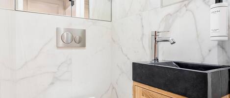 A modern bathroom with a marble wall, a black sink, and a toilet.