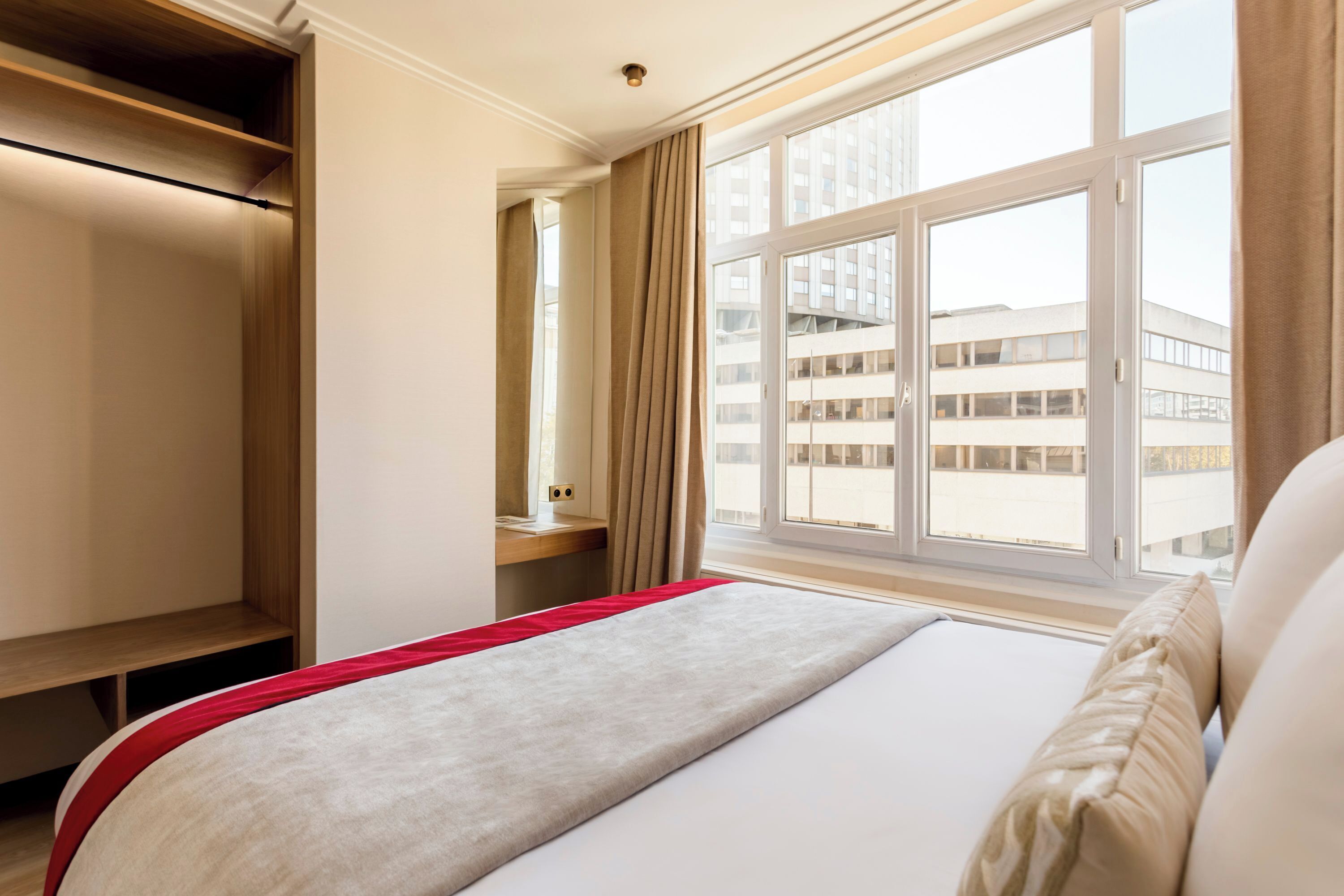 A hotel room with a bed, a desk, and a window with a view of a building.