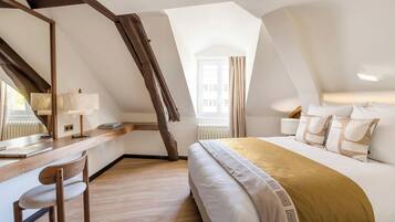 A bedroom with a sloped ceiling, a bed with a patterned throw, a desk with a chair, and a window with curtains.
