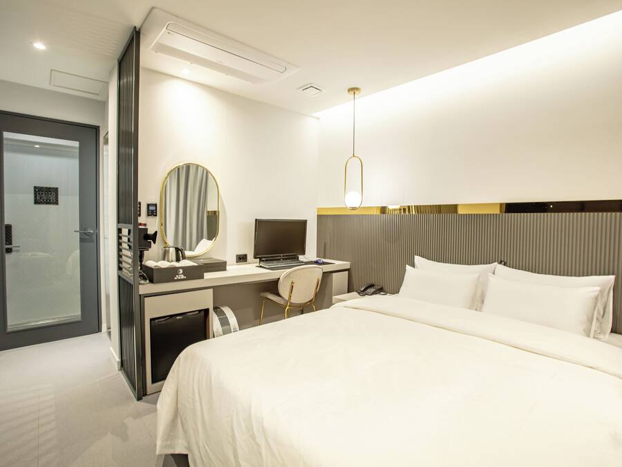 A modern hotel room with a bed, desk, chair, and a large mirror.