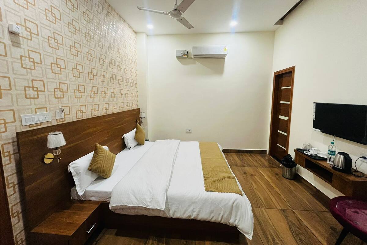 A hotel room with a bed, a ceiling fan, an air conditioning unit, a TV, and a wooden floor.