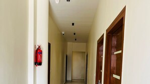 Ein Korridor mit an der Wand montiertem Feuerlöscher, Holztüren und gefliestem Boden.