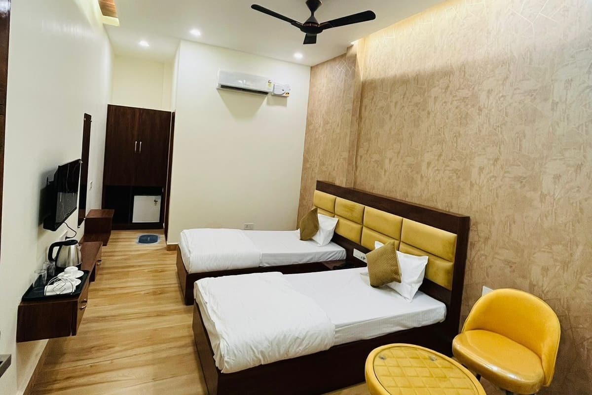 A hotel room with two beds, a ceiling fan, an air conditioning unit, a television, and a small seating area with yellow chairs.