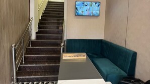 Eine moderne Hotellobby mit einem geometrisch gemusterten Boden, einer Treppe mit Metallgeländer, einem türkisfarbenen Sofa und einer an der Wand befestigten Überwachungskamera.