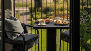 Ein Balkon mit einem Frühstückstisch, einem Korbstuhl und Blick auf ein Wohngebäude.
