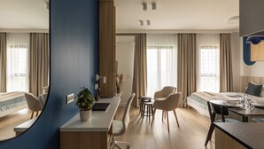 Ein modernes Hotelzimmer mit einer zentralen Essecke, einem Bett mit Blick und einem großen Fenster mit Vorhängen.