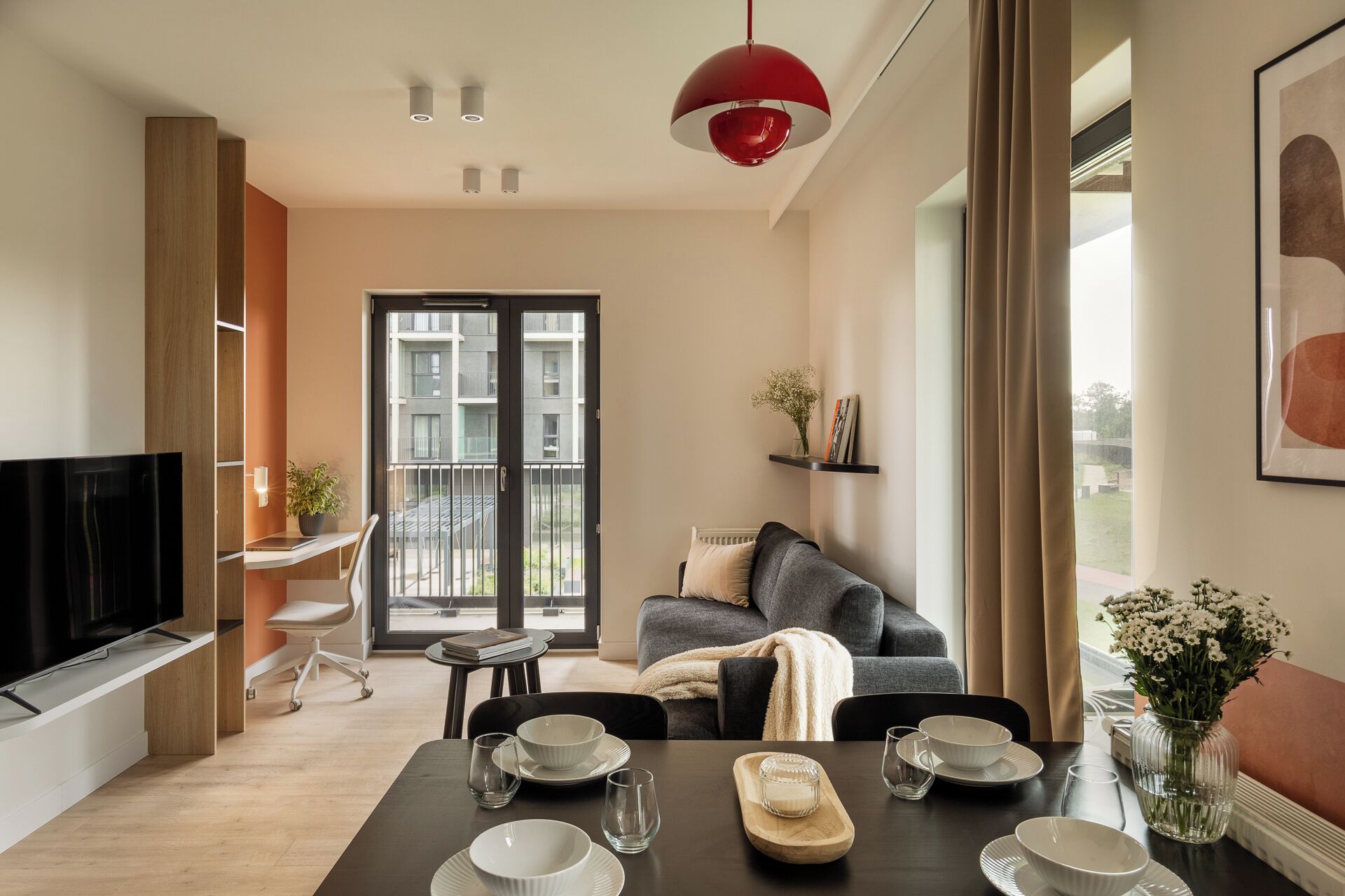 A modern living room with a dining area, a television, and a balcony with a view of the building.