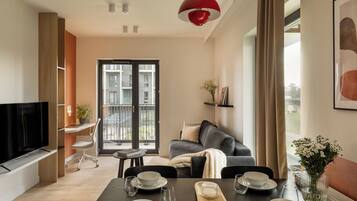 A modern living room with a dining area, a television, and a balcony with a view of the building.