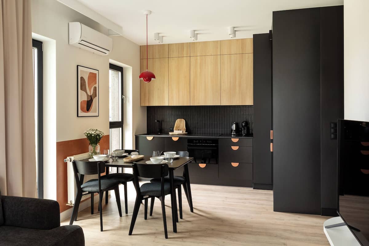 A modern kitchen with wooden cabinets, a black countertop, and a dining area with a table and chairs.