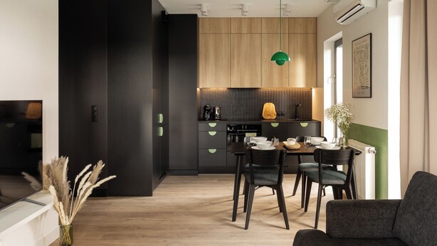 Eine moderne Küche mit Holzschränken, einer Essecke mit zwei Stühlen und einer grünen Pendelleuchte.