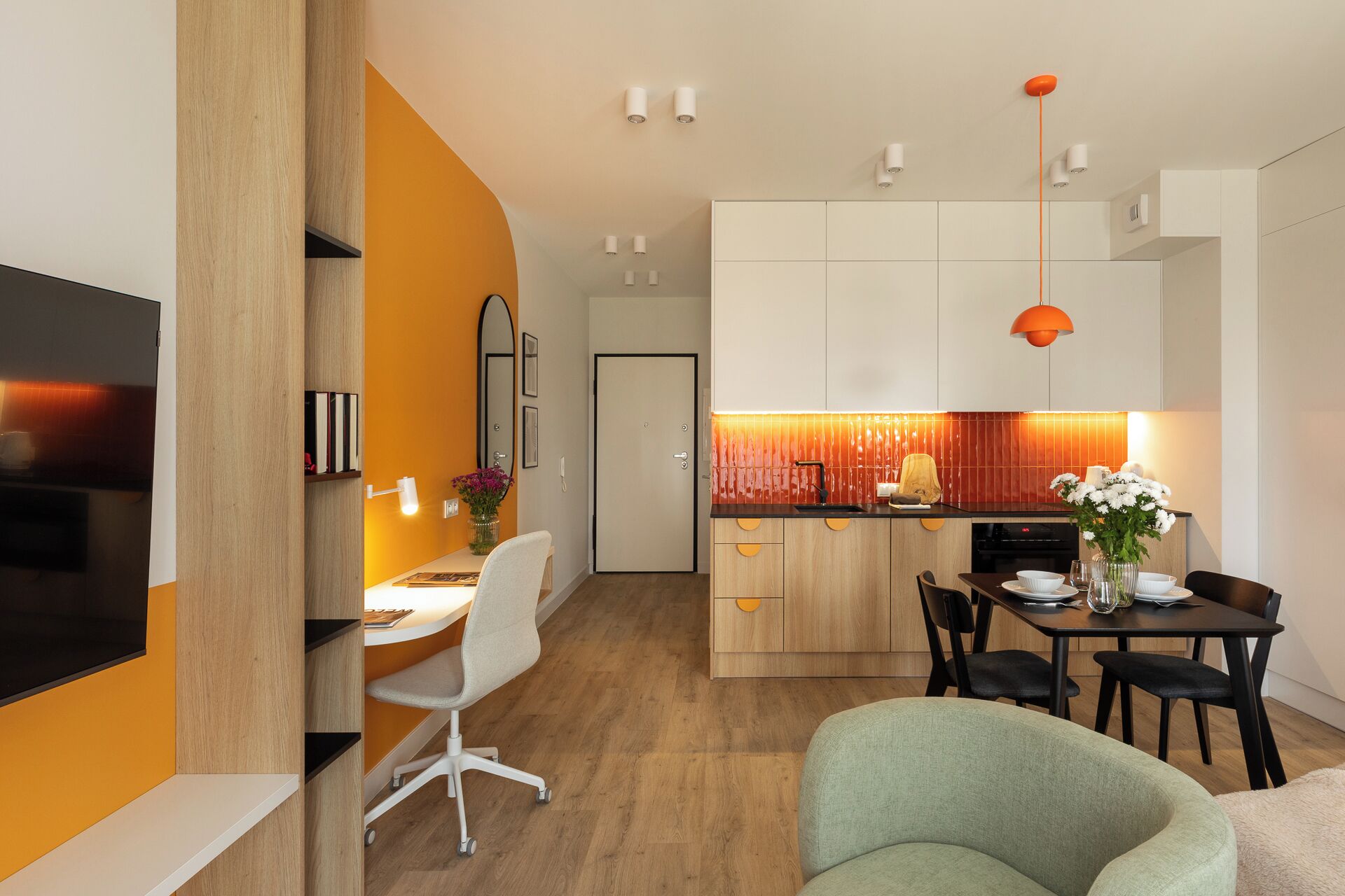 A modern kitchen with a dining area, featuring a wooden floor, white cabinets, and a central island with a sink.