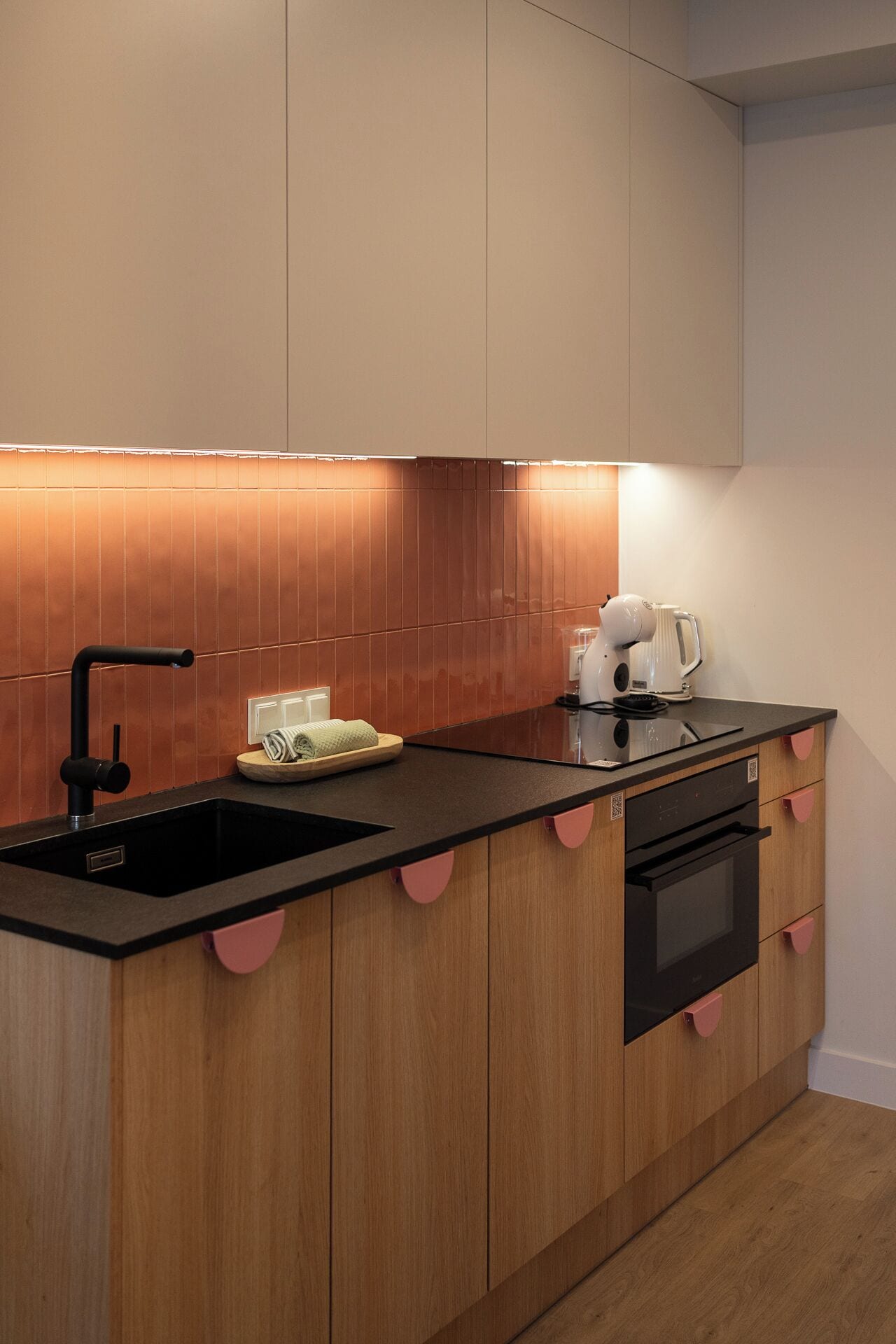 A modern kitchen with a black countertop, wooden cabinets, a sink, a kettle, and a built-in oven.