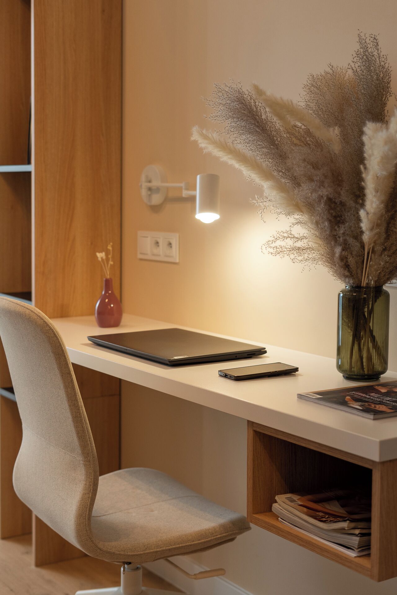 A modern workspace with a laptop, smartphone, and decorative vase on a white desk.