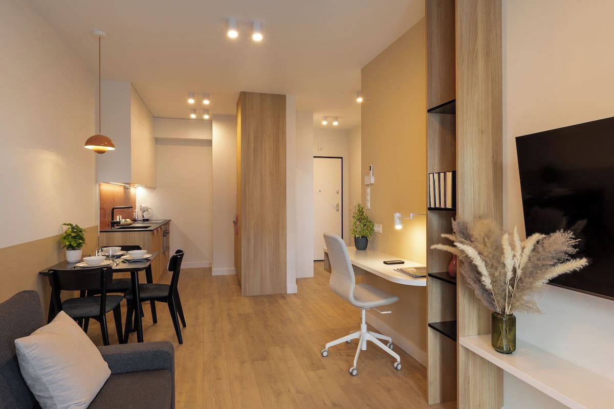 A modern living room with a sofa, a dining table with chairs, a TV mounted on the wall, and a wooden floor.