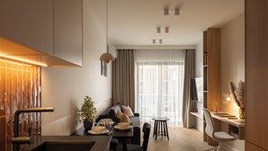 Eine moderne Küche mit Einbauherd, eine Essecke mit Tisch und Stühlen, eine Couch und ein an der Wand befestigter Fernseher.