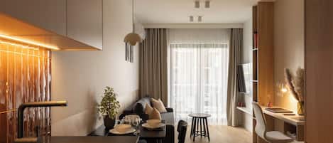 A modern kitchen with a built-in stove, a dining area with a table and chairs, a sofa, and a TV mounted on the wall.