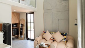 A modern living room with a sofa, a coffee table, and a colorful rug. There is a staircase leading to an upper level. - Chunnchay Bed&Restaurant (Mae Wang)