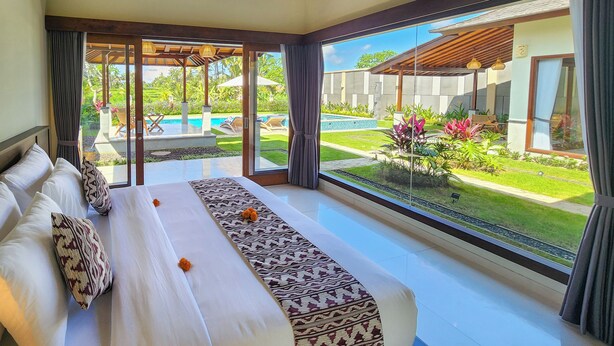 Amplia habitación con una cama grande, vista a una piscina y un jardín cuidado.