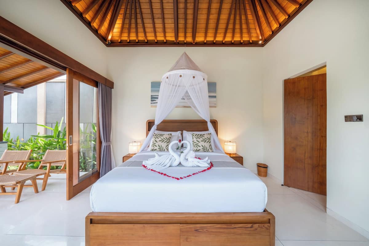 A bedroom with a canopy bed, a view of the garden, and a wooden ceiling.