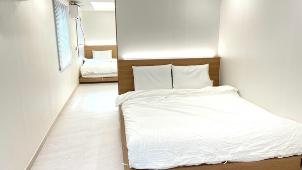Ett modernt hotellrum med en sängram i trä, vita sängkläder och ett stort fönster med persienner.