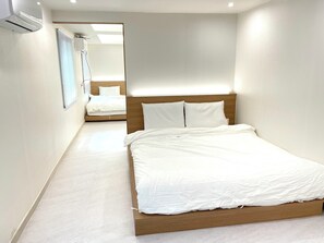Quarto de hotel moderno com estrutura de cama em madeira, roupa de cama branca e uma janela grande com persianas.